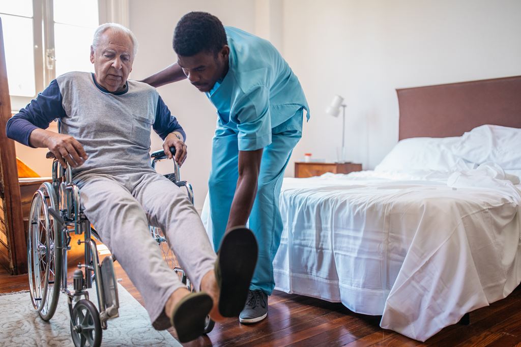 Man nurse helping senior in wheelchair in nursing home.