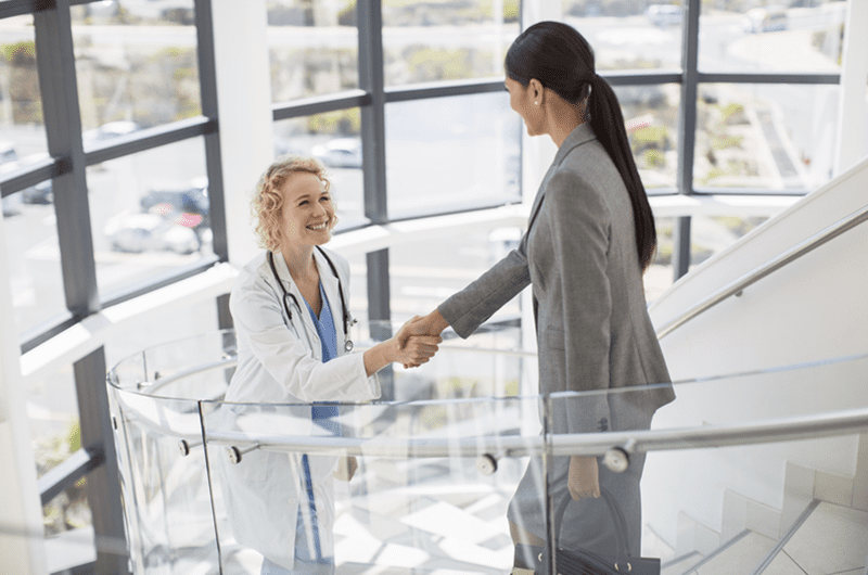 Image of female doctor and businesswoman shaking hands on stairs