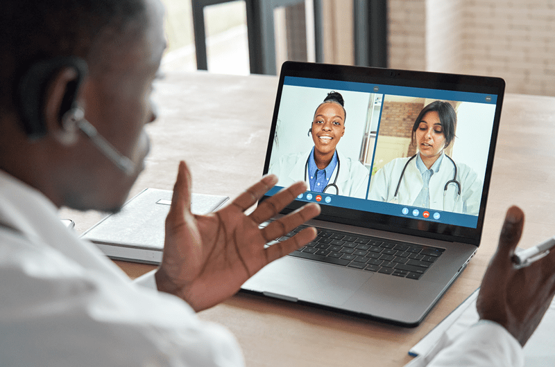 A medical professional speaking to two other medical professionals on a laptop screen.